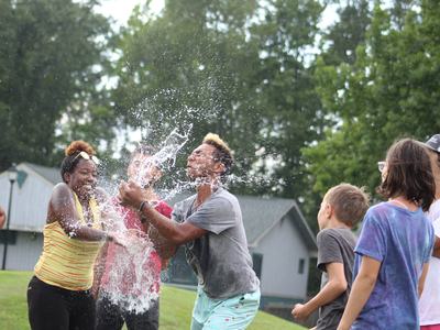 Teenagers outdoors splashing water; water hitting a young man's face