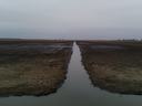 Water-filled drainage ditch running through plowed field to the horizon
