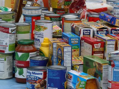 Assorted canned goods, boxed pasta mixes, jars, and condiments arranged on a table