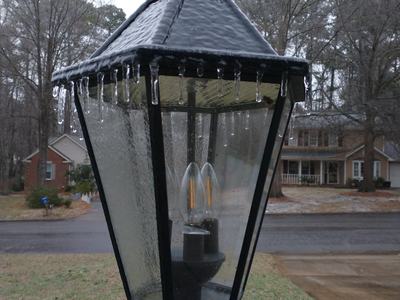 glaze of ice and small icicles hanging from the top edge of a yard lamp