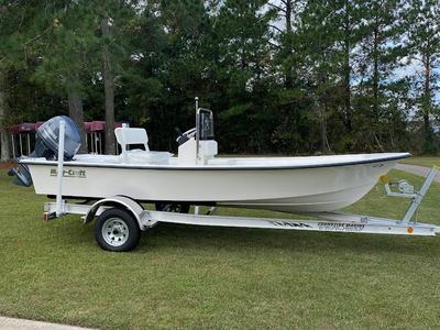 White center-console skiff on a trailer parked on grass with trees in background