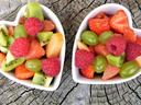 Two heart-shaped bowls of mixed fruit (strawberries, raspberries, kiwi, grapes) on a tree stump