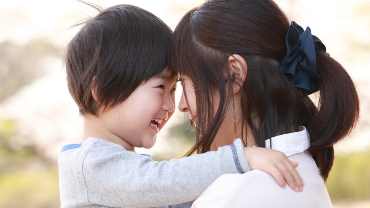Child smiling with forehead touching adult's, arms around adult's shoulders