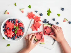 Hands cutting star-shaped watermelon pieces with cutter; bowl of stars and blueberries