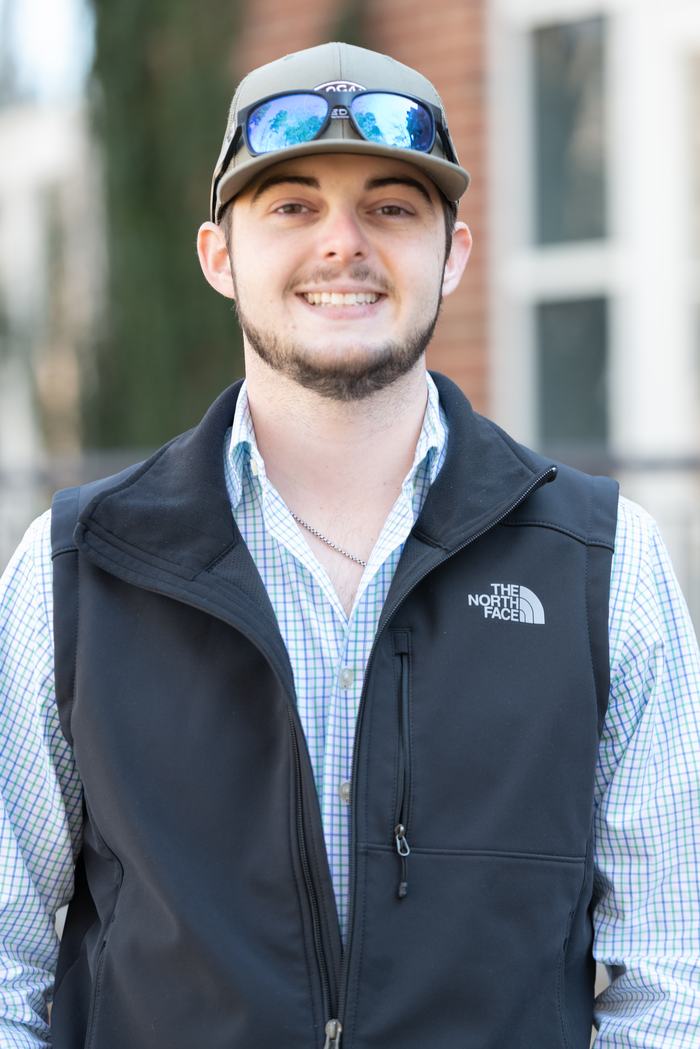 Young man wearing a cap, reflective sunglasses, and black vest with "The North Face" logo