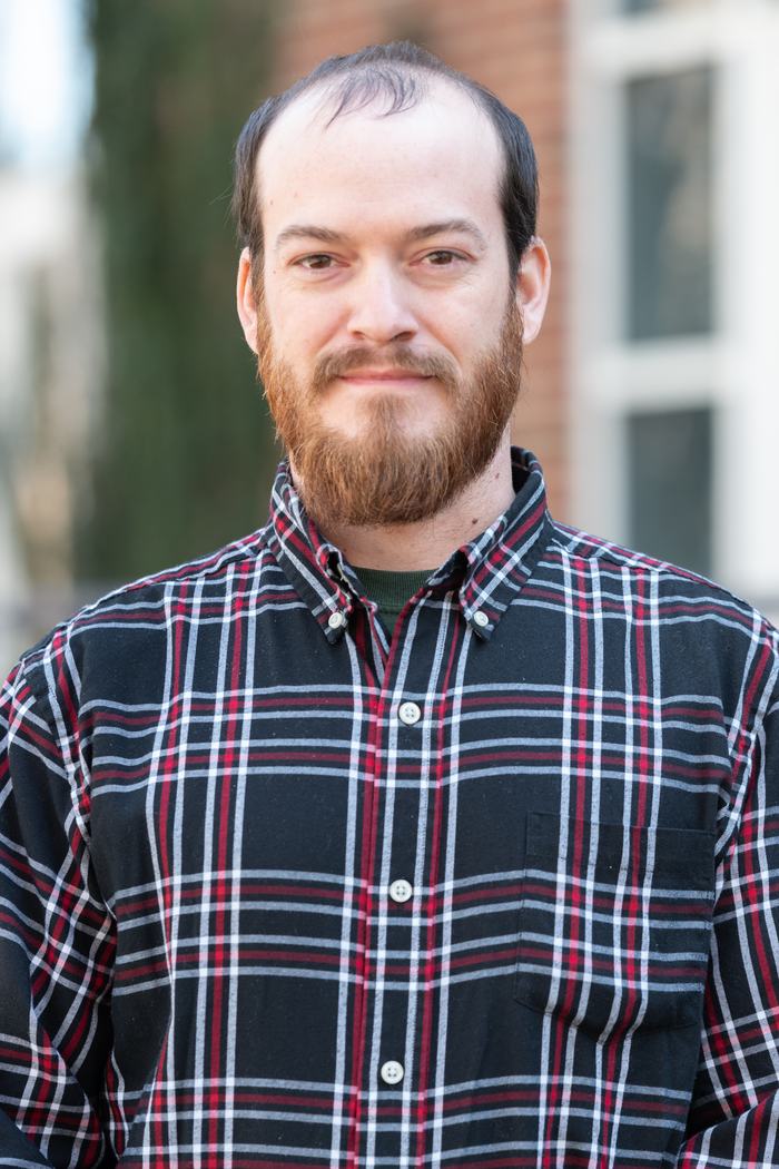 Bearded man wearing black red plaid button-up shirt standing outdoors