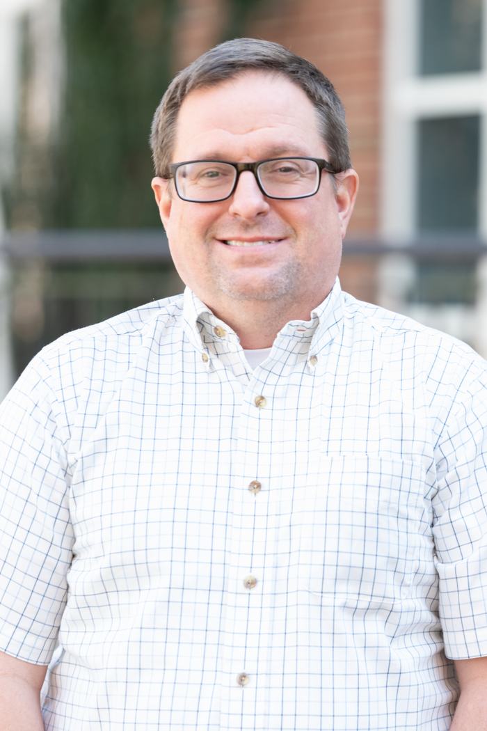 Middle-aged man with glasses wearing a white checkered button-down shirt outdoors