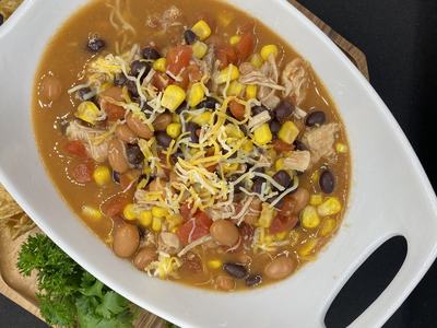White serving dish with chicken tortilla soup: corn, black and pinto beans, tomatoes, shredded cheese