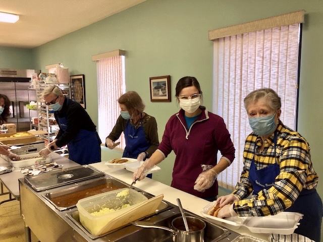 Volunteers wearing masks and gloves serving food into takeout containers