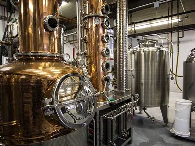 Copper pot still with column and stainless steel fermentation tanks in a distillery