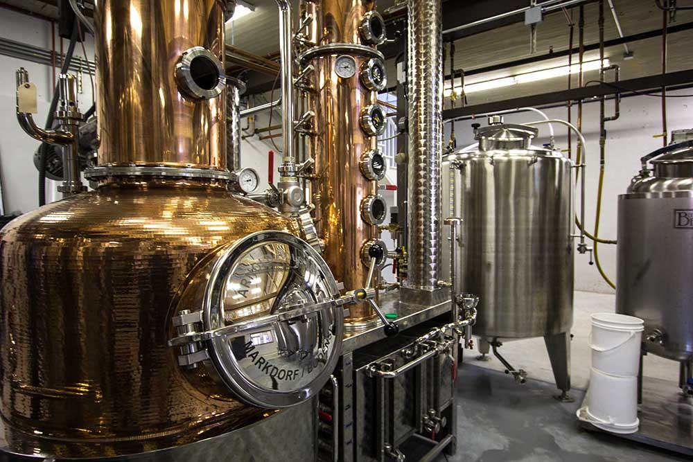 Copper pot still with column and stainless steel fermentation tanks in a distillery