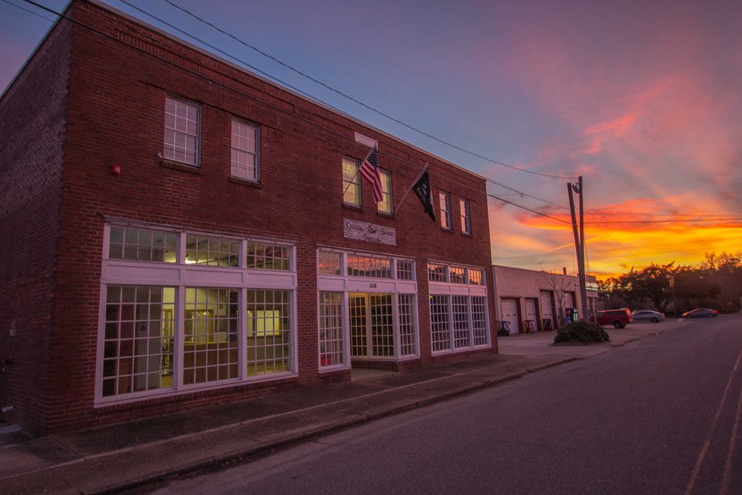 Two-story brick commercial building with American and black flags, sunset sky