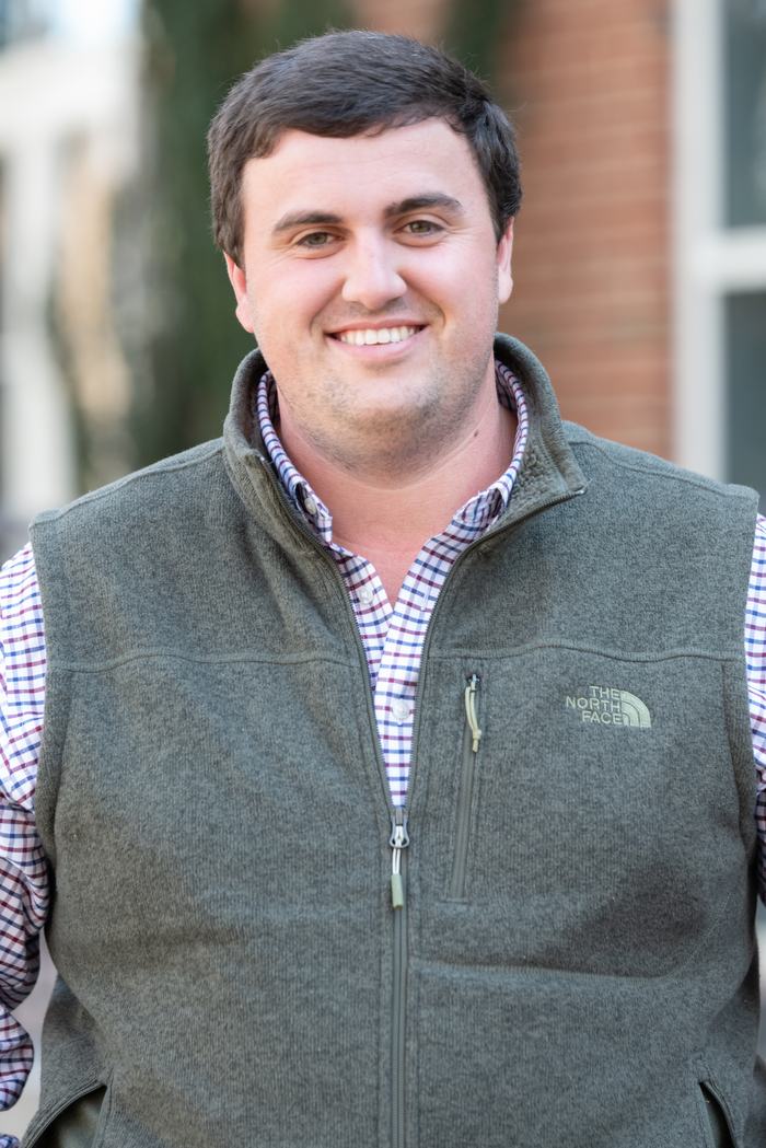 Man wearing green vest with "THE NORTH FACE" logo and checked shirt, smiling outdoors