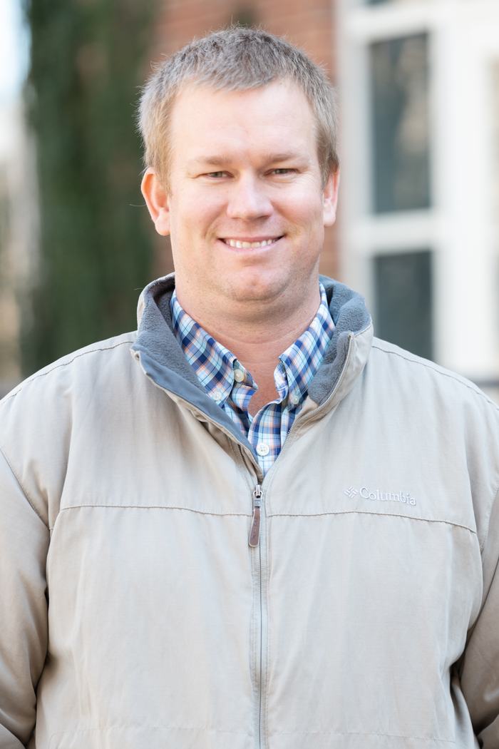 Man wearing beige Columbia jacket and plaid shirt, standing outdoors