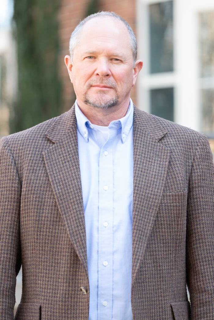 Man in brown houndstooth blazer and light blue button-down shirt standing outdoors