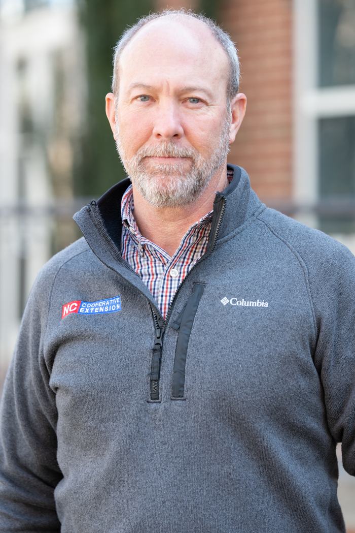 Adult man wearing gray Columbia pullover with NC Cooperative Extension patch, outdoors.