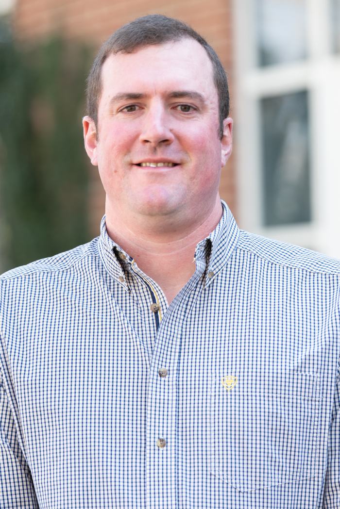 Adult man facing camera wearing a blue checkered button-down shirt
