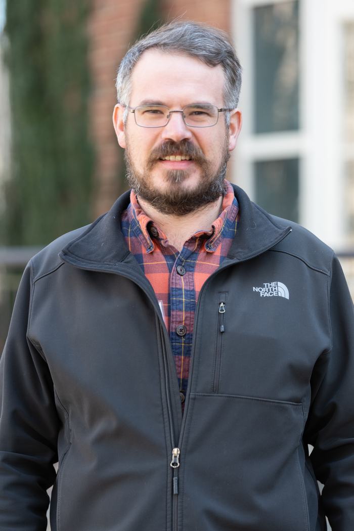 Bearded man wearing glasses, plaid shirt, and black jacket with The North Face logo