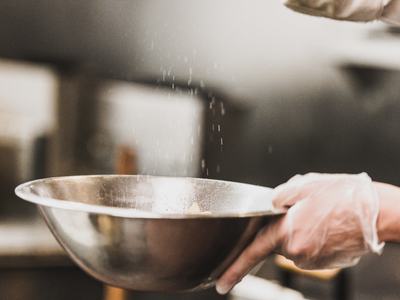 Gloved hands sprinkling spices in bowl.