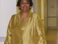 Woman standing in a hallway wearing a gold jacket and blouse