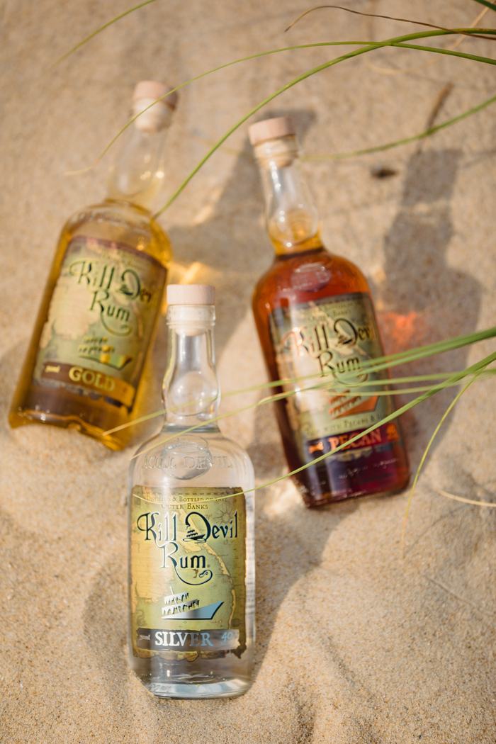 Three Kill Devil Rum bottles lying on sand, foreground bottle labeled "Silver"