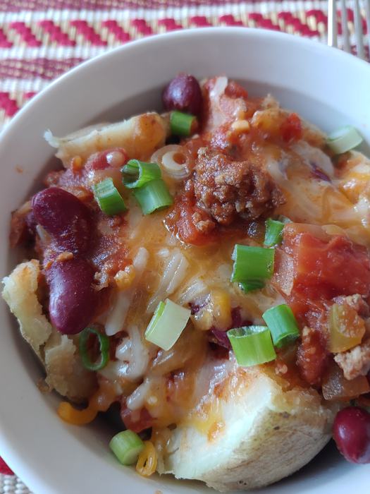Baked potato topped with chili, kidney beans, melted cheese, and chopped green onions