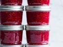 Eight glass jars of raspberry jam stacked in two columns, raspberries and mint at base.