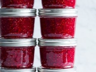 Eight glass jars of raspberry jam stacked in two columns, raspberries and mint at base.