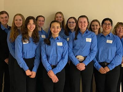 Twelve people in matching blue button-down shirts and black pants with name tags, standing