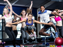 Five people jumping during a group fitness class in a gym, using step platforms