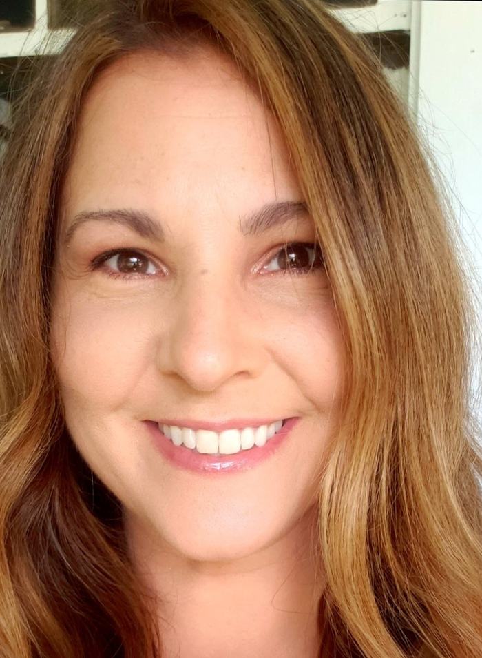 Close-up of a woman smiling with long brown hair and visible upper teeth
