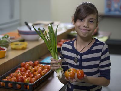 Young girl holding green onions and tomatoes at a produce counter
