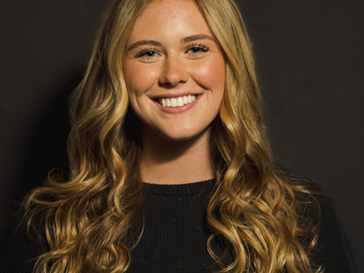 Young woman with long wavy blonde hair smiling against a dark background