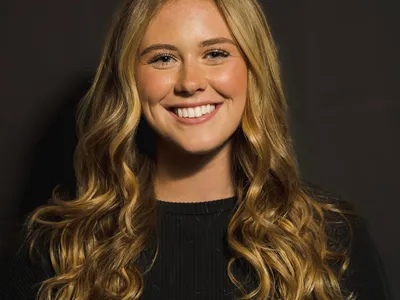 Young woman with long wavy blonde hair smiling against a dark background