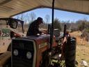 Man leaning over red Massey Ferguson 240 tractor under metal shelter; skid-steer 753 nearby