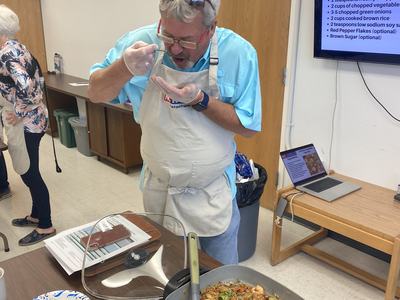 Man in apron tasting shrimp fried rice from a skillet in a classroom kitchen