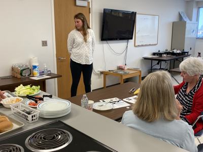 Woman standing by door addressing seated people in a community kitchen/classroom
