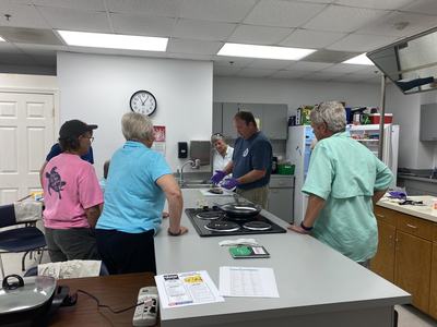 Group of adults around kitchen counter watching a man wearing purple gloves prepare food
