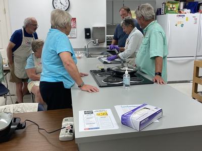Group of adults gathered around a kitchen counter while one person wearing purple gloves handles food