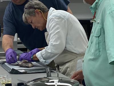 Three people wearing gloves and aprons filleting a fish on a kitchen counter
