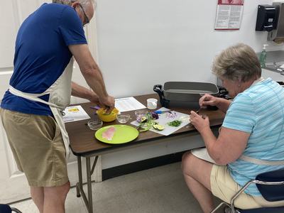 Two people wearing aprons preparing food at a table, chopping herbs and fish.