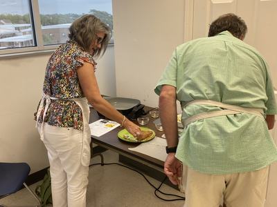Two people in aprons preparing food on a table with plates and small bowls