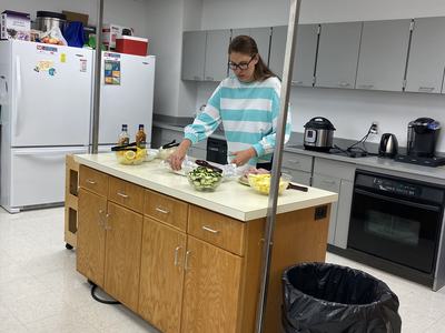 Person in striped shirt cutting vegetables on a kitchen island in a kitchen/breakroom