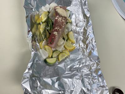Raw fish fillet with sliced zucchini, yellow squash, onion and herbs on aluminum foil