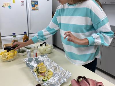 Person arranging lemon-topped fish and vegetables on aluminum foil on kitchen counter