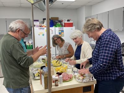 Five adults preparing food at a kitchen island with bowls, lemon slices, and foil