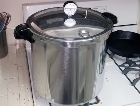 Stainless steel pressure canner with lid and dial thermometer on gas stovetop