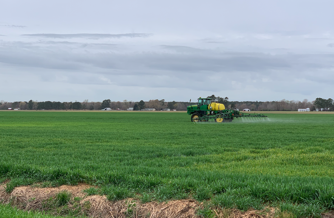 Self-propelled sprayer spraying a green crop field under cloudy sky