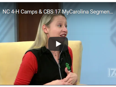 Woman wearing 4‑H vest speaking on TV set; onscreen text: "NC 4-H Camps & CBS 17 MyCarolina Segment"