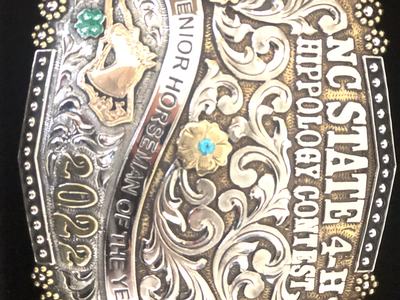 Silver and gold belt buckle reading "NC STATE 4-H HIPP OLOGY CONTEST" and "Senior Horseman of the Year 2022"